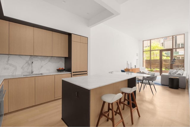 kitchen with light brown cabinets, a sink, a kitchen breakfast bar, backsplash, and a center island