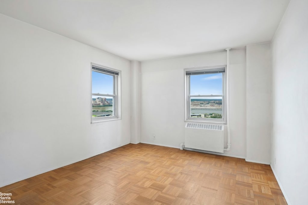 empty room with light parquet flooring, radiator, and plenty of natural light