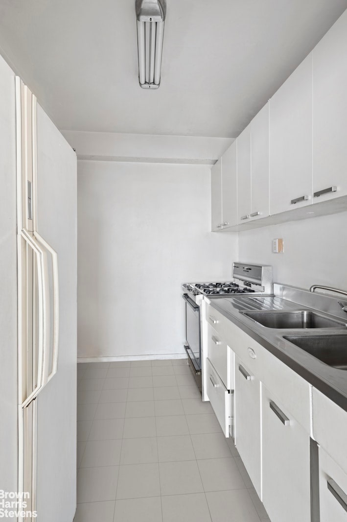 kitchen featuring tile patterned floors, white cabinetry, freestanding refrigerator, baseboards, and stainless steel range with gas stovetop