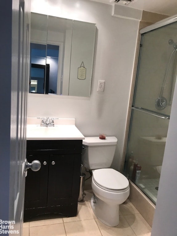 bathroom with a shower with shower door, vanity, tile patterned floors, and toilet