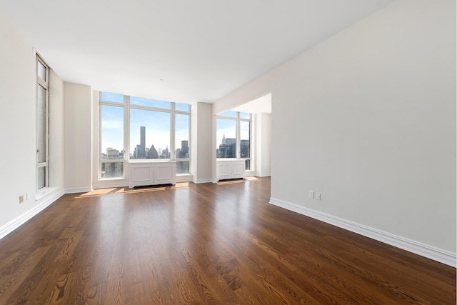 unfurnished living room with a view of city, expansive windows, dark wood-style flooring, and baseboards