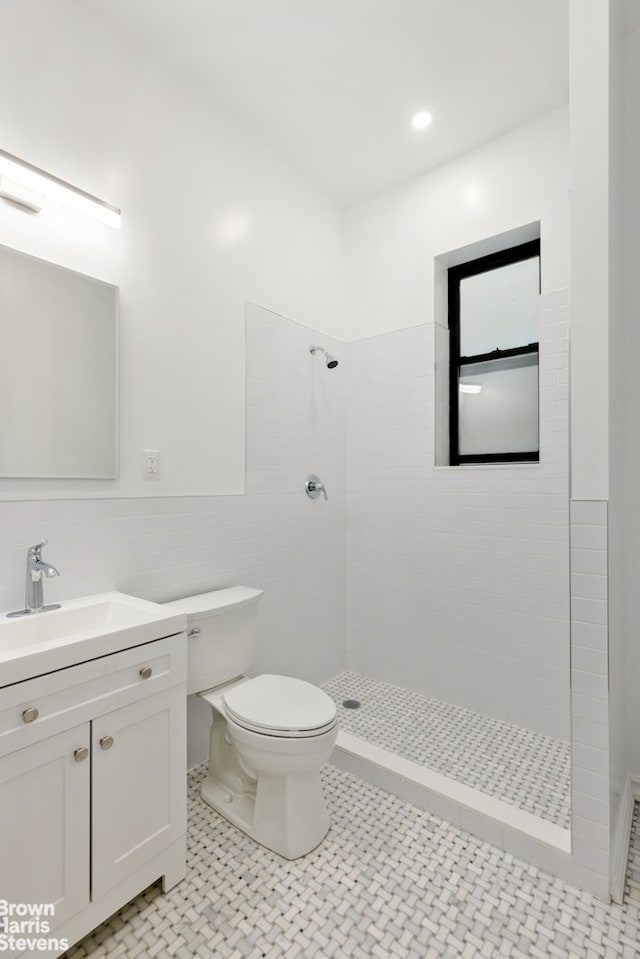 full bath with a tile shower, tile walls, toilet, and vanity