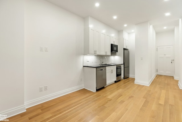 kitchen featuring black appliances, light wood-style flooring, white cabinetry, and backsplash