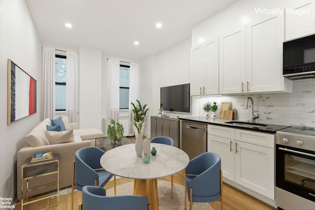 kitchen featuring backsplash, appliances with stainless steel finishes, white cabinetry, a sink, and light wood-type flooring