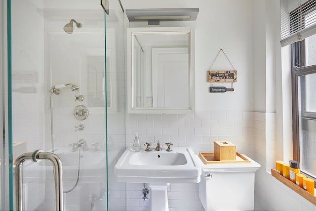 bathroom with a shower with door, sink, tile walls, and toilet