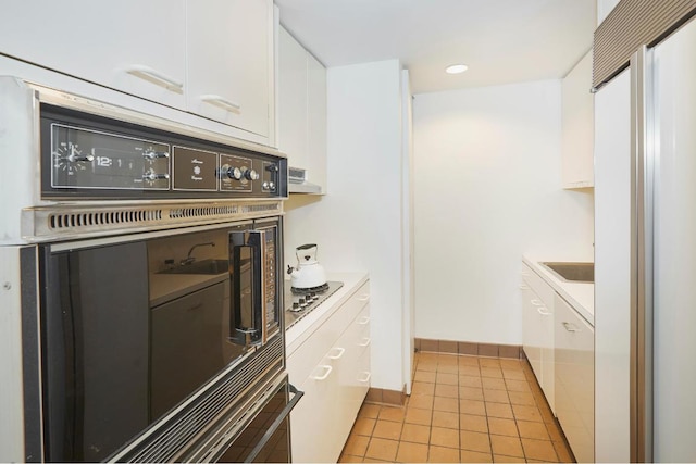 kitchen featuring stainless steel gas stovetop, light tile patterned floors, white cabinets, and black oven