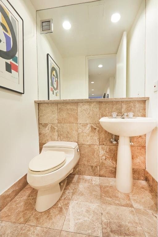 bathroom featuring toilet and tile walls