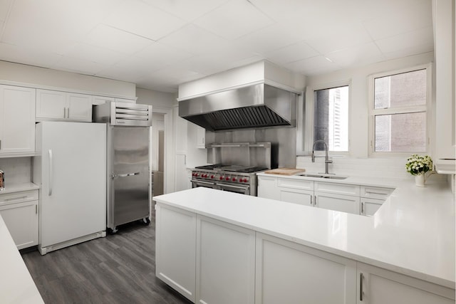 kitchen featuring wall chimney range hood, tasteful backsplash, a sink, freestanding refrigerator, and dark wood-style floors