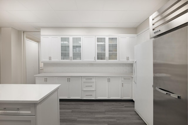 kitchen with dark wood finished floors, light countertops, white cabinets, freestanding refrigerator, and glass insert cabinets