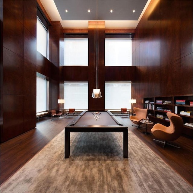 game room with wood walls, plenty of natural light, a towering ceiling, and wood finished floors