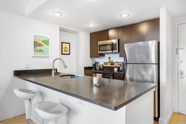 kitchen featuring light hardwood / wood-style floors, kitchen peninsula, sink, stainless steel appliances, and dark brown cabinets