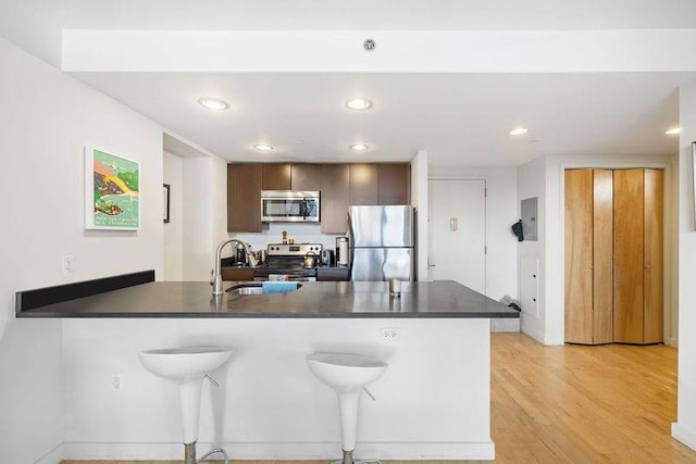 kitchen featuring sink, light hardwood / wood-style flooring, a breakfast bar area, appliances with stainless steel finishes, and kitchen peninsula