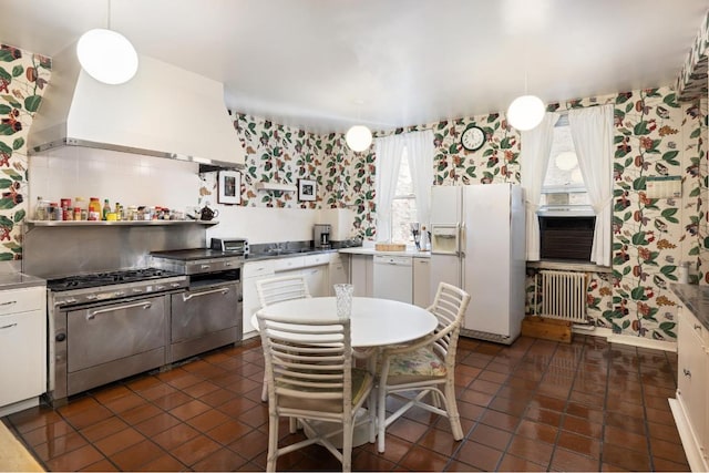 kitchen with white appliances, white cabinets, radiator heating unit, wall chimney exhaust hood, and hanging light fixtures