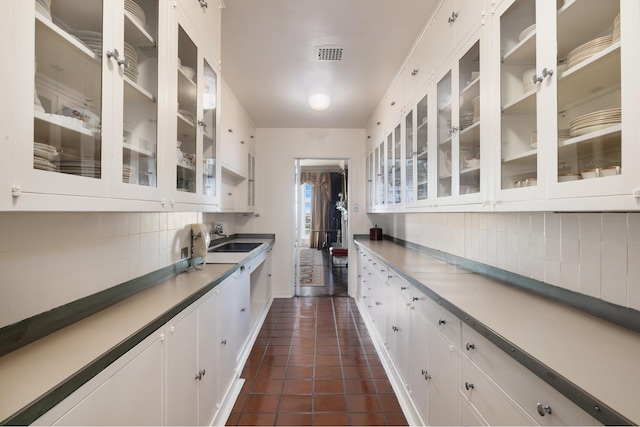 kitchen featuring a sink, visible vents, white cabinetry, decorative backsplash, and dark tile patterned flooring
