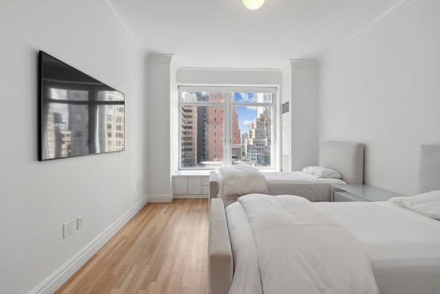 bedroom featuring light wood finished floors, baseboards, ornamental molding, and a city view