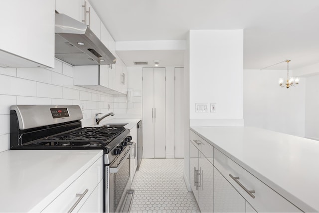 kitchen featuring tasteful backsplash, light countertops, a sink, under cabinet range hood, and stainless steel gas range oven