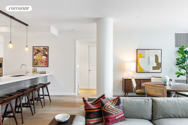 living room featuring light wood-type flooring, decorative columns, visible vents, and baseboards