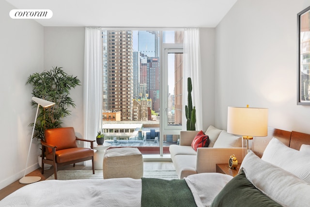 sitting room with baseboards, visible vents, wood finished floors, a wall of windows, and a city view