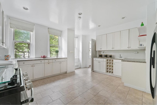 kitchen featuring light stone countertops, stainless steel range, white cabinetry, sink, and light tile patterned flooring