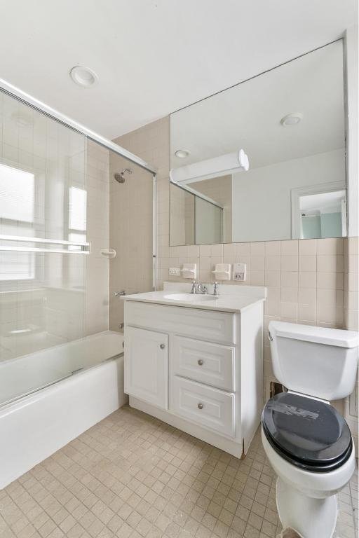 full bathroom with toilet, enclosed tub / shower combo, tasteful backsplash, tile walls, and vanity