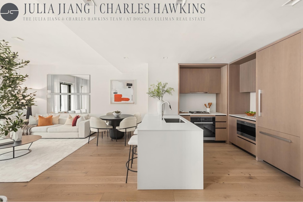200 E 21st St Unit 6D, New York City, NY 10010 - kitchen featuring light countertops, black oven, modern cabinets, a kitchen breakfast bar, and light wood-style flooring