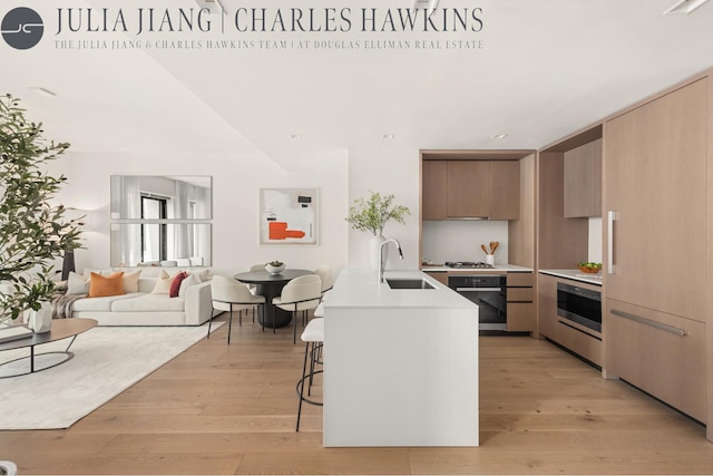 200 E 21st St Unit 6D, New York City, NY 10010 - kitchen featuring light countertops, black oven, modern cabinets, a kitchen breakfast bar, and light wood-style flooring