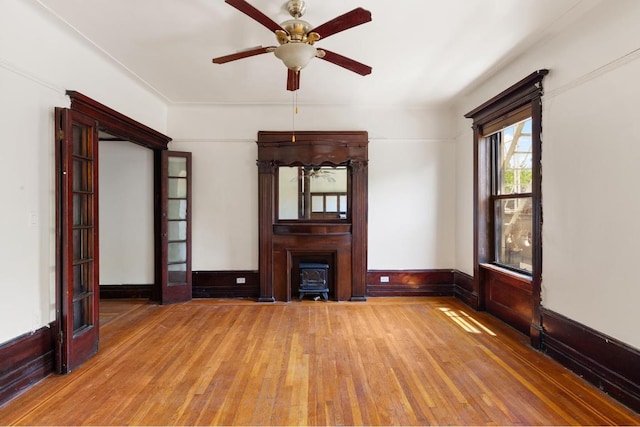 unfurnished living room with ceiling fan, hardwood / wood-style floors, and a wood stove