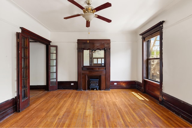 unfurnished living room featuring ceiling fan, hardwood / wood-style floors, wainscoting, and a wood stove