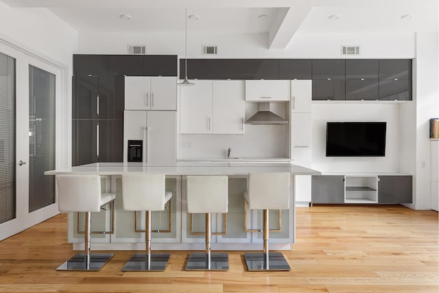 315 7th Ave Unit 3D, New York City, NY 10001 - kitchen featuring a kitchen breakfast bar, light wood finished floors, light countertops, wall chimney range hood, and hanging light fixtures
