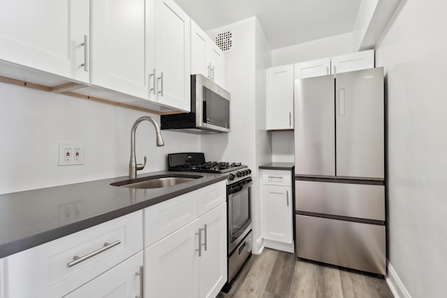 kitchen featuring wood finished floors, a sink, white cabinets, appliances with stainless steel finishes, and dark countertops