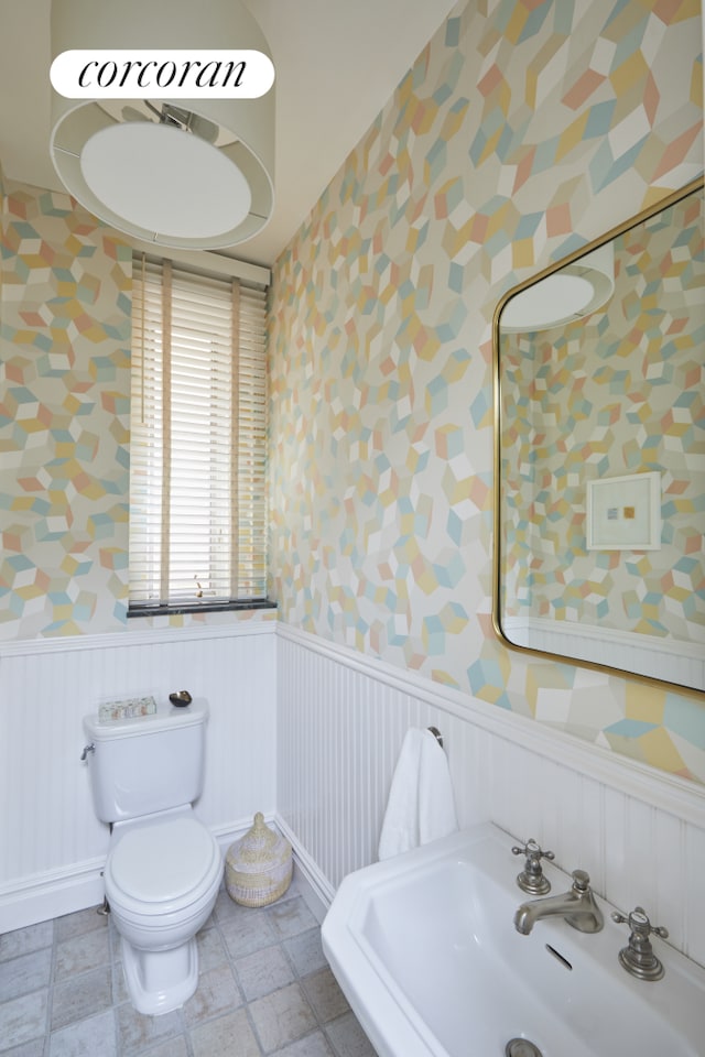 bathroom with a sink, a wainscoted wall, toilet, and wallpapered walls