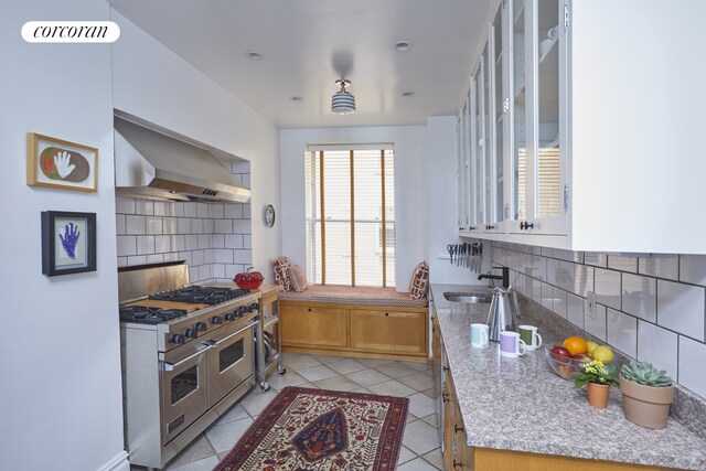 kitchen with light tile patterned floors, tasteful backsplash, wall chimney exhaust hood, double oven range, and a sink