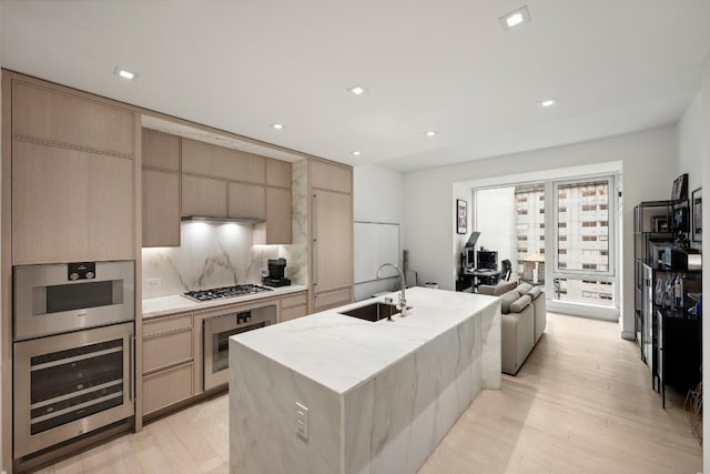 kitchen featuring backsplash, sink, an island with sink, light brown cabinets, and stainless steel appliances