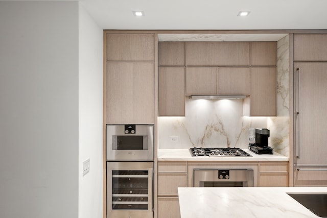 kitchen with light brown cabinetry, backsplash, stainless steel gas stovetop, and wine cooler