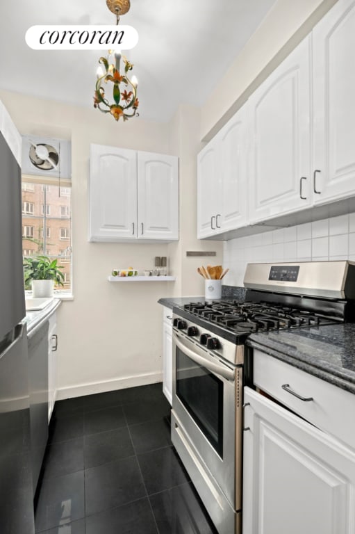 kitchen with dark tile patterned floors, gas stove, decorative backsplash, and white cabinets