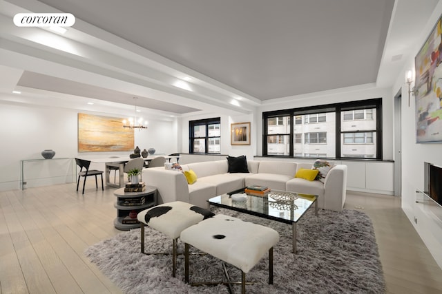 living area featuring a tray ceiling, visible vents, light wood finished floors, and an inviting chandelier