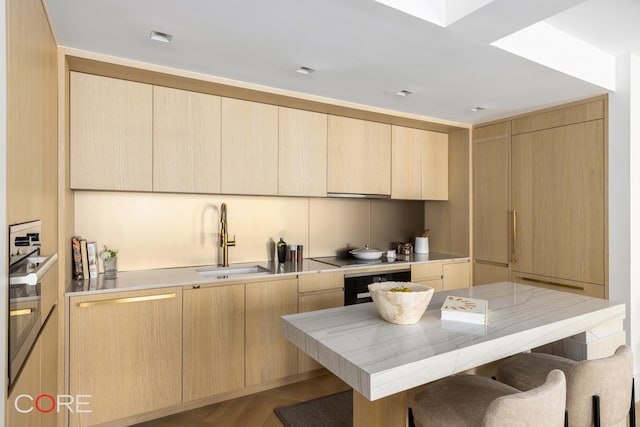 kitchen with light brown cabinetry, a breakfast bar area, a sink, and oven