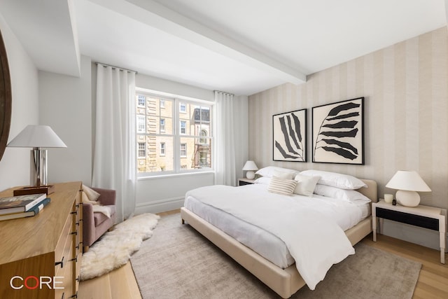 bedroom with wood finished floors, beamed ceiling, baseboards, and wallpapered walls