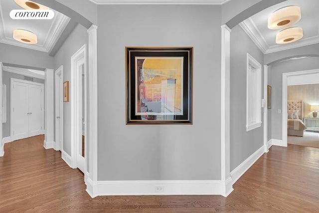 hall with wood-type flooring, crown molding, and decorative columns