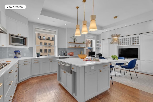 kitchen featuring stainless steel microwave, a center island, light hardwood / wood-style floors, pendant lighting, and a tray ceiling