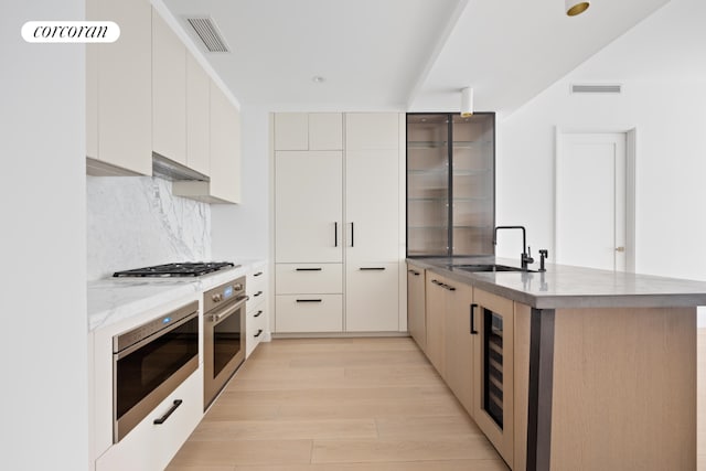 kitchen featuring appliances with stainless steel finishes, sink, wine cooler, backsplash, and light wood-type flooring