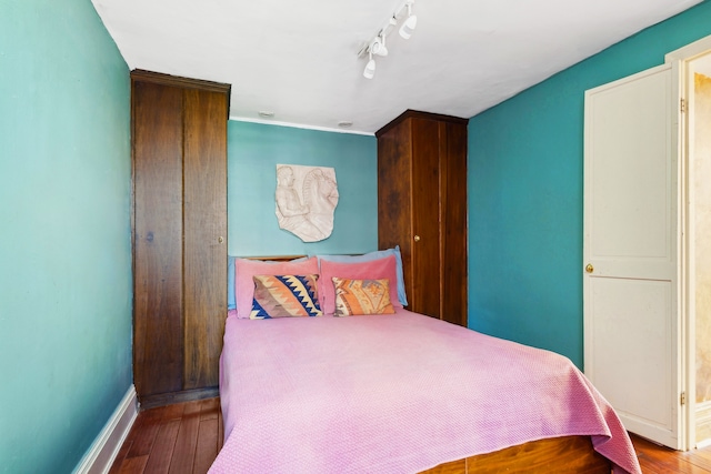 bedroom with baseboards, wood finished floors, and track lighting