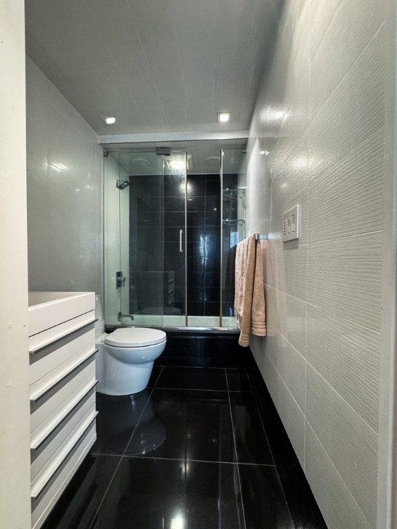 bathroom featuring toilet, bath / shower combo with glass door, and tile walls