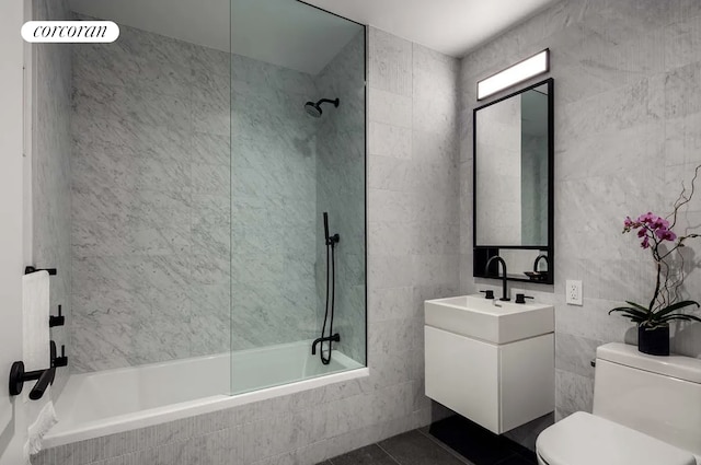 full bathroom featuring tiled shower / bath, toilet, vanity, and tile walls