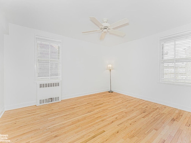 spare room with radiator, light wood finished floors, ceiling fan, and baseboards