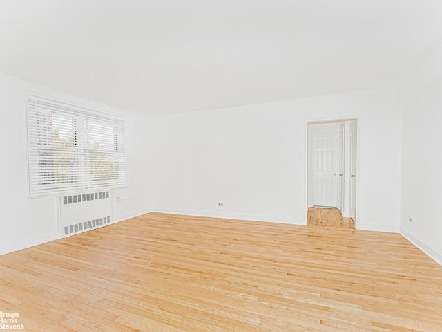 empty room featuring baseboards, light wood-type flooring, and radiator