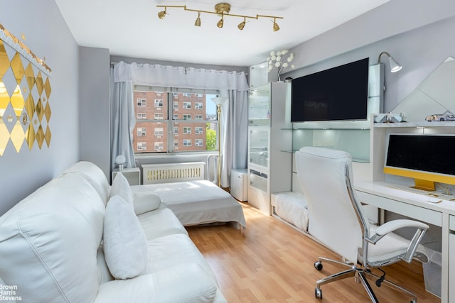 bedroom featuring rail lighting, wood finished floors, and radiator heating unit