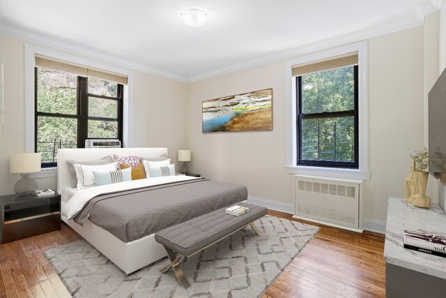 bedroom with multiple windows, radiator heating unit, light wood-style flooring, and crown molding