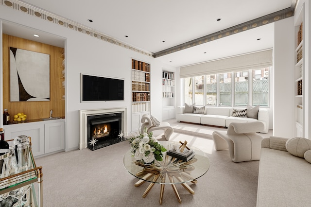 living area featuring built in features, carpet, a warm lit fireplace, and ornamental molding