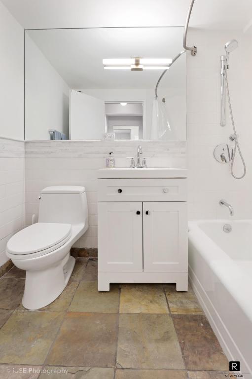 full bathroom with tile walls, toilet, vanity, and shower / tub combo